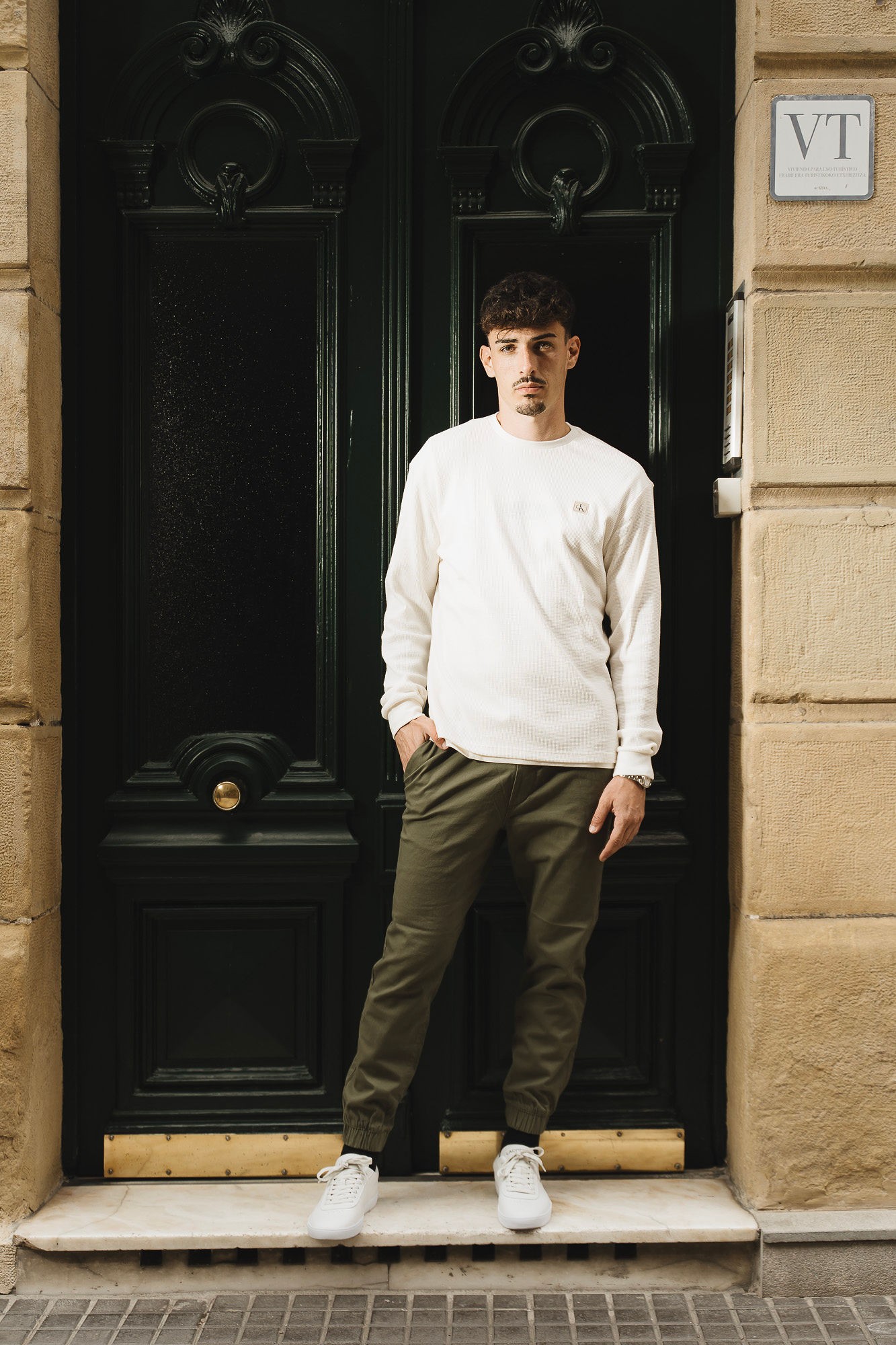 Look de hombre con jersey blanco roto, camiseta básica y pantalones chinos verde militar