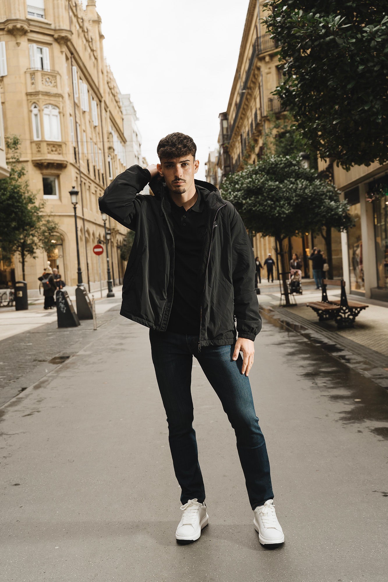Look urbano de hombre con cazadora negra, vaqueros oscuros y zapatillas blancas