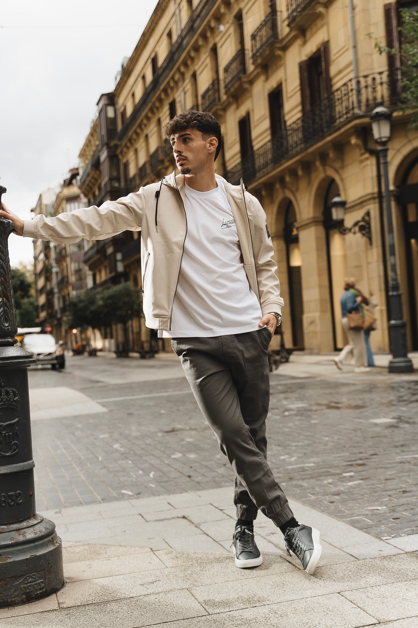 Look de hombre con camiseta blanca, cazadora beige y pantalón chino gris oscuro